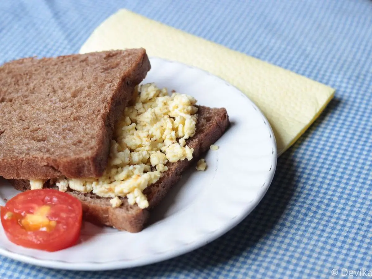 Rebanadas de pan tostado con huevo revuelto y medio tomate en un plato sobre mantel de cuadros azules