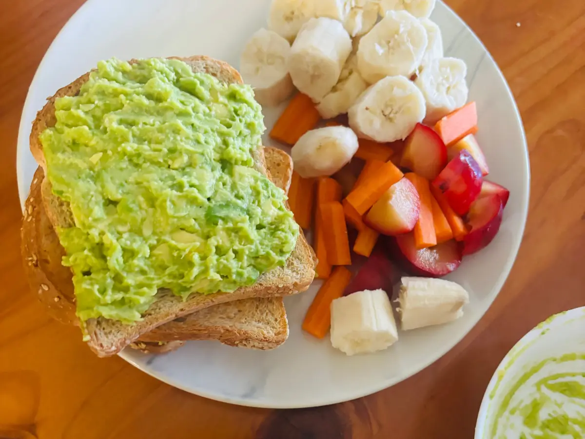Tostada con aguacate machacado junto a fruta troceada