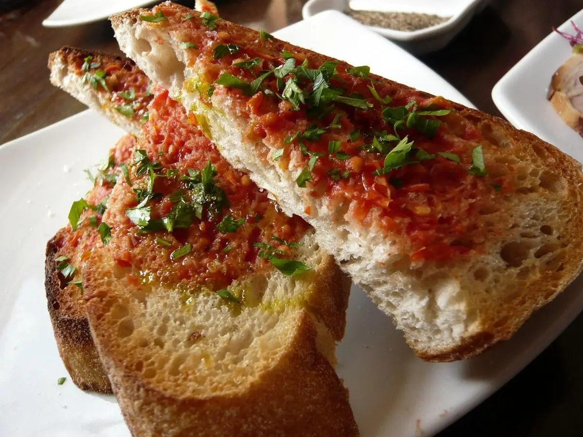Rebanadas gruesas de pan rústico tostado con tomate rallado, aceite y perejil picado en un plato blanco