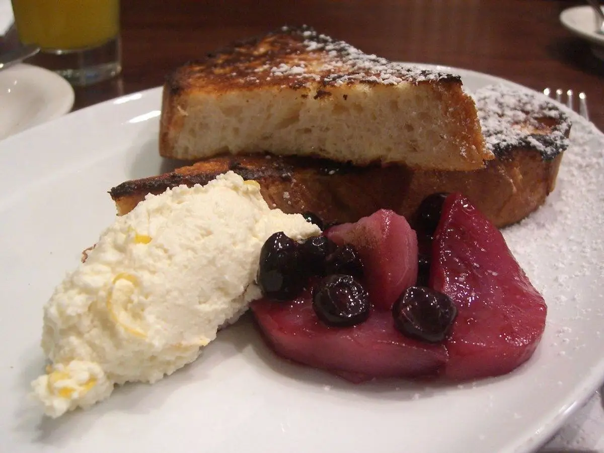 Torrija de pan tostado con crema blanca y frutos rojos en un plato blanco