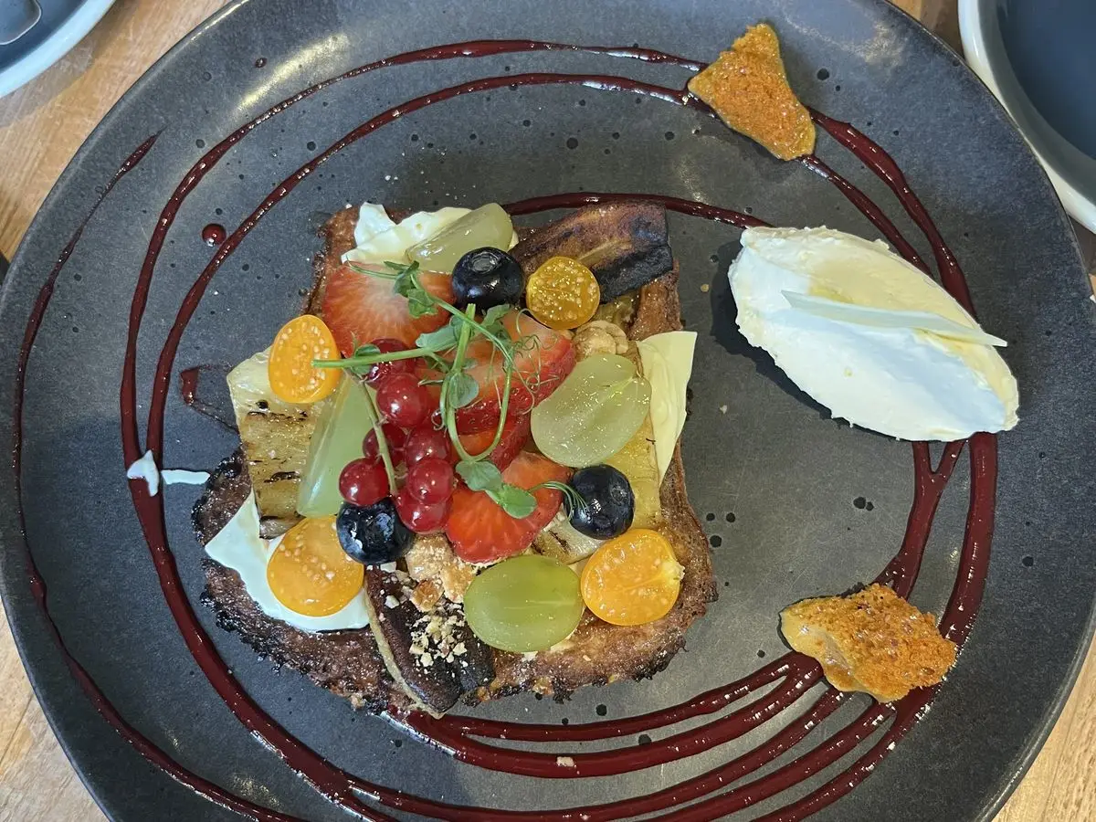Tostada cubierta de fresas, arándanos, uvas y physalis con un poco de nata en un plato oscuro