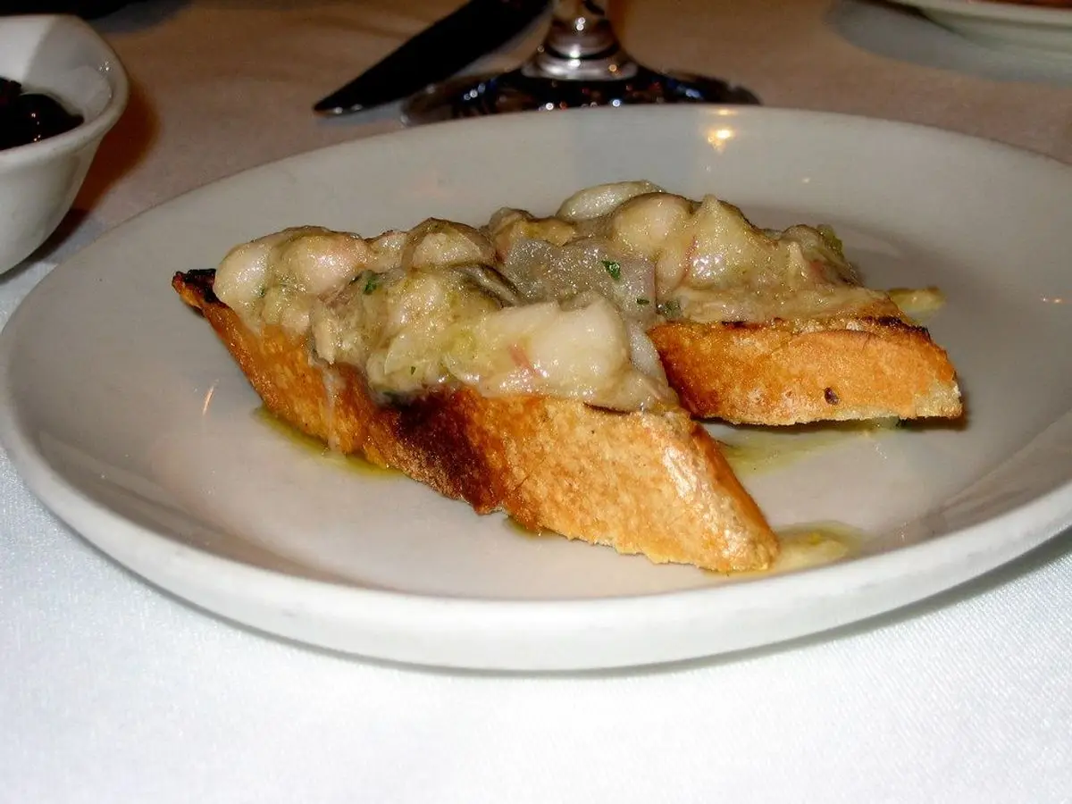 Rebanadas de pan tostado cubiertas con alubias blancas cremosas y hierbas en un plato blanco