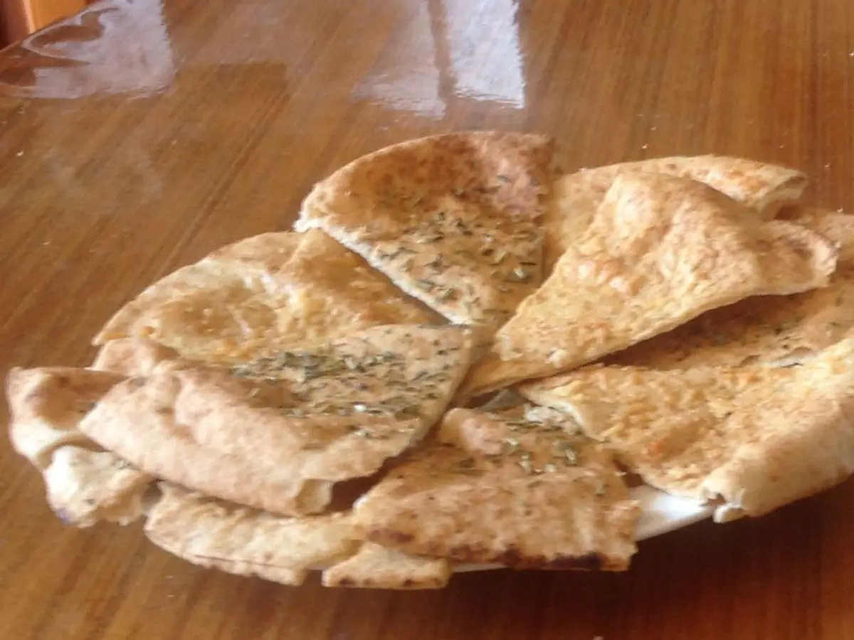 Triángulos de pan de pita tostado junto a un cuenco con salsa blanca de yogur