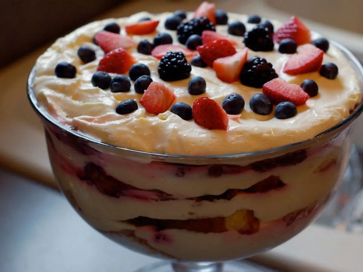 Copa de cristal de trifle con capas de crema, bizcocho y frutos rojos y arándanos por encima