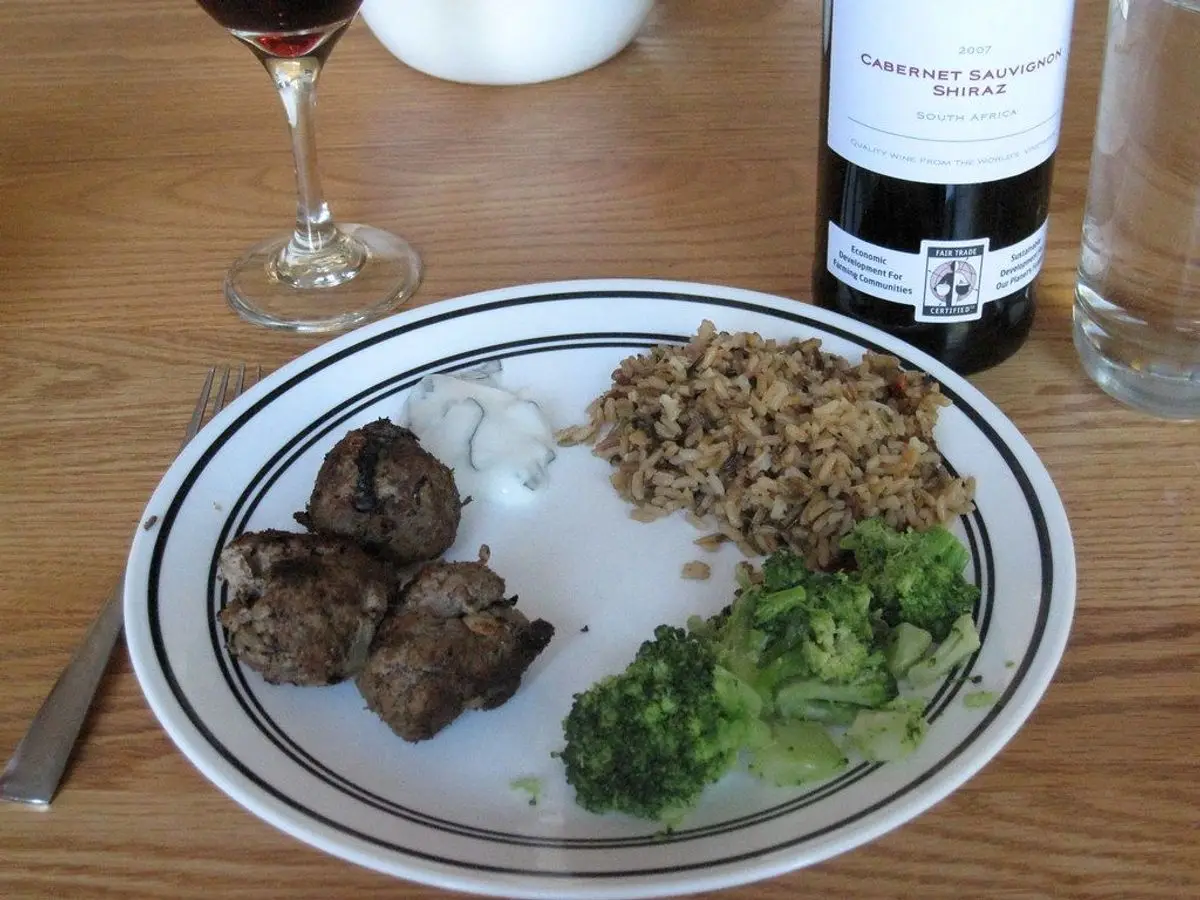 Plato con albóndigas de carne, arroz integral o cereal en grano y brócoli sobre mesa de madera