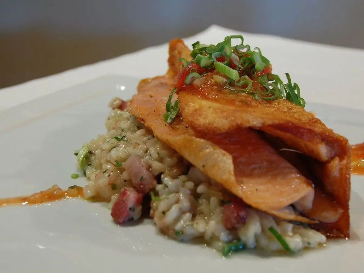 Filete de pescado dorado y crujiente sobre arroz con tropezones de jamón