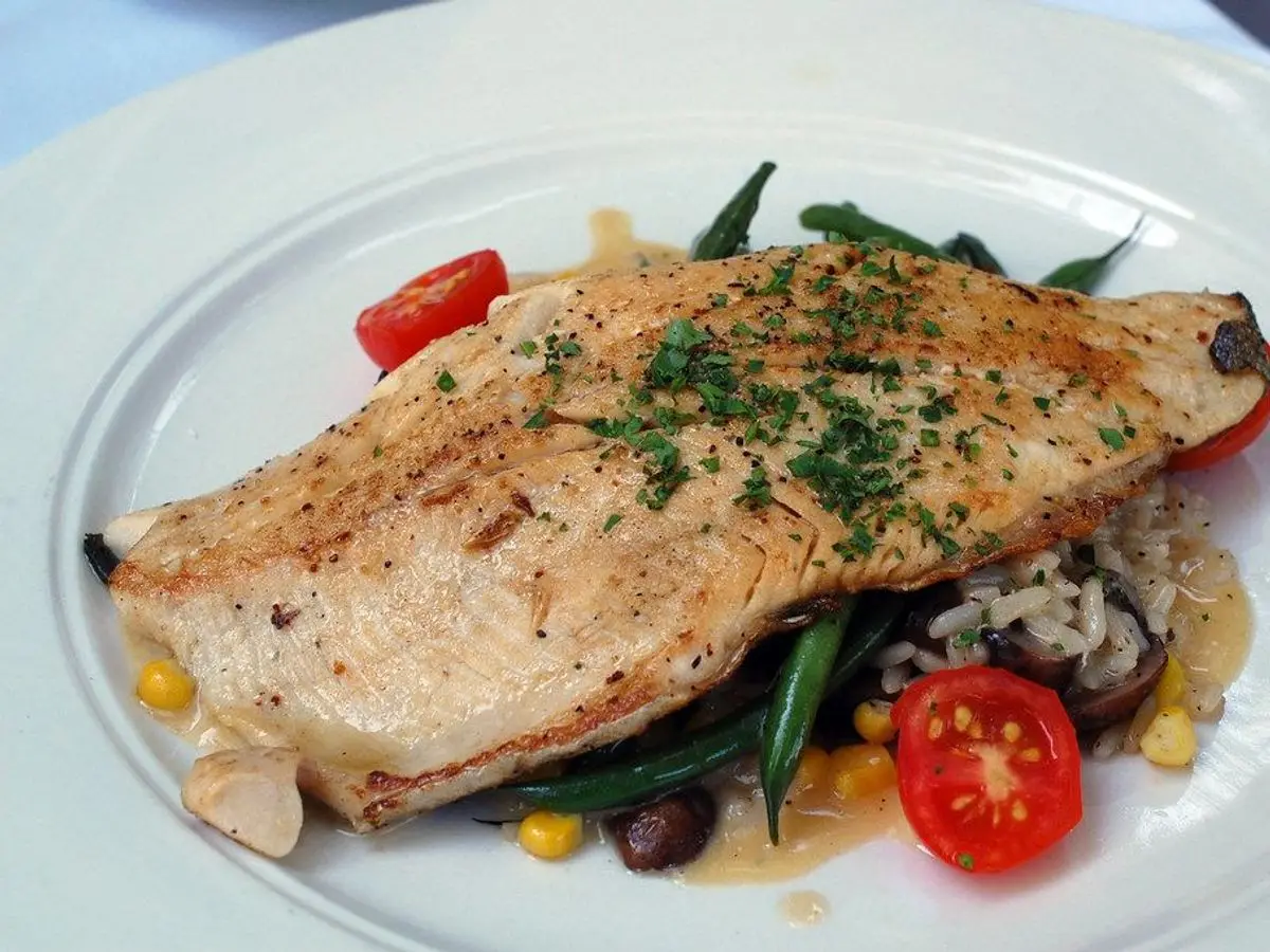 Filete de trucha dorado sobre judías verdes, maíz y tomate cherry en un plato blanco