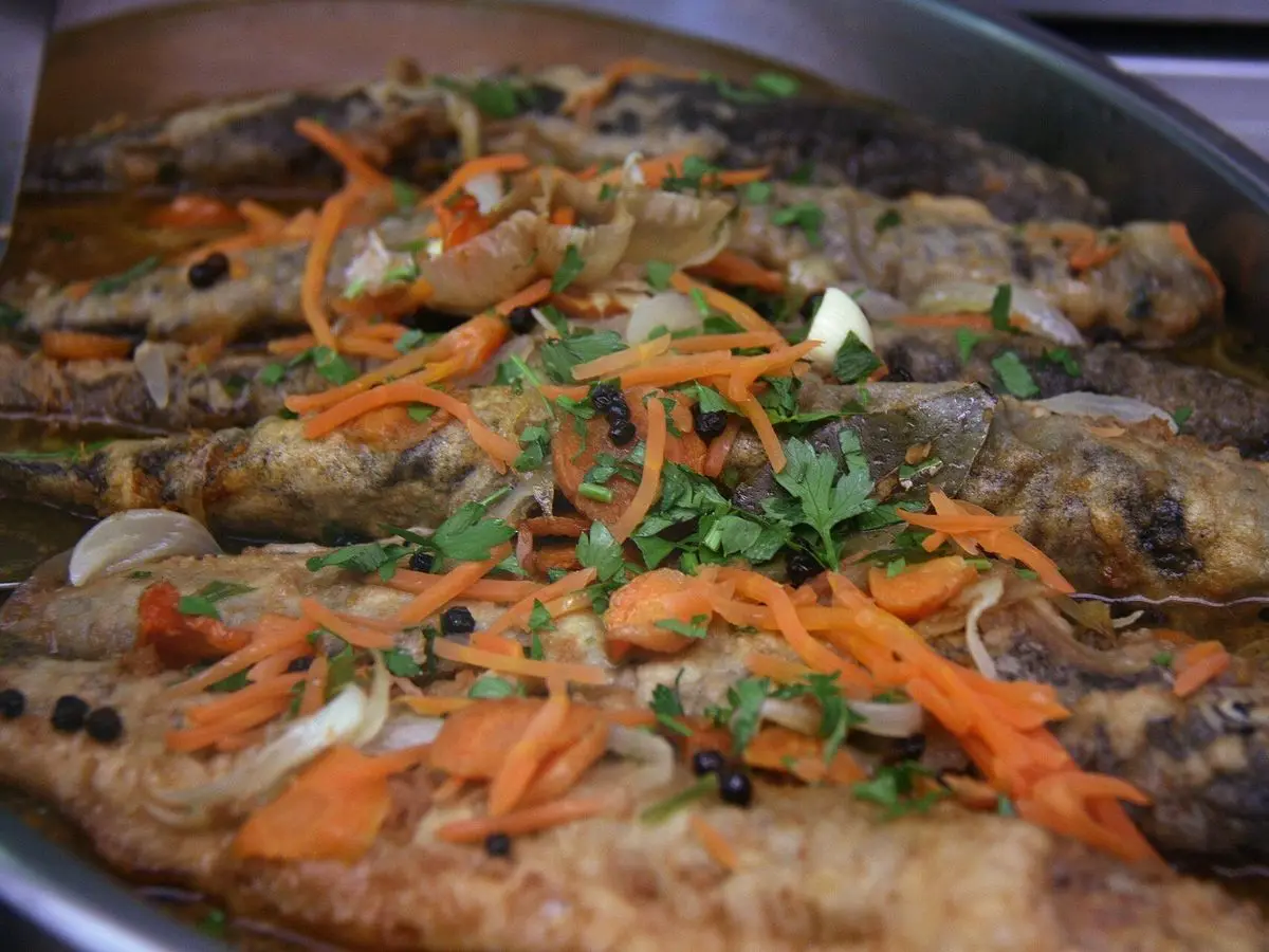 Bandeja de truchas en escabeche cubiertas de zanahoria en tiras, cebolla y perejil