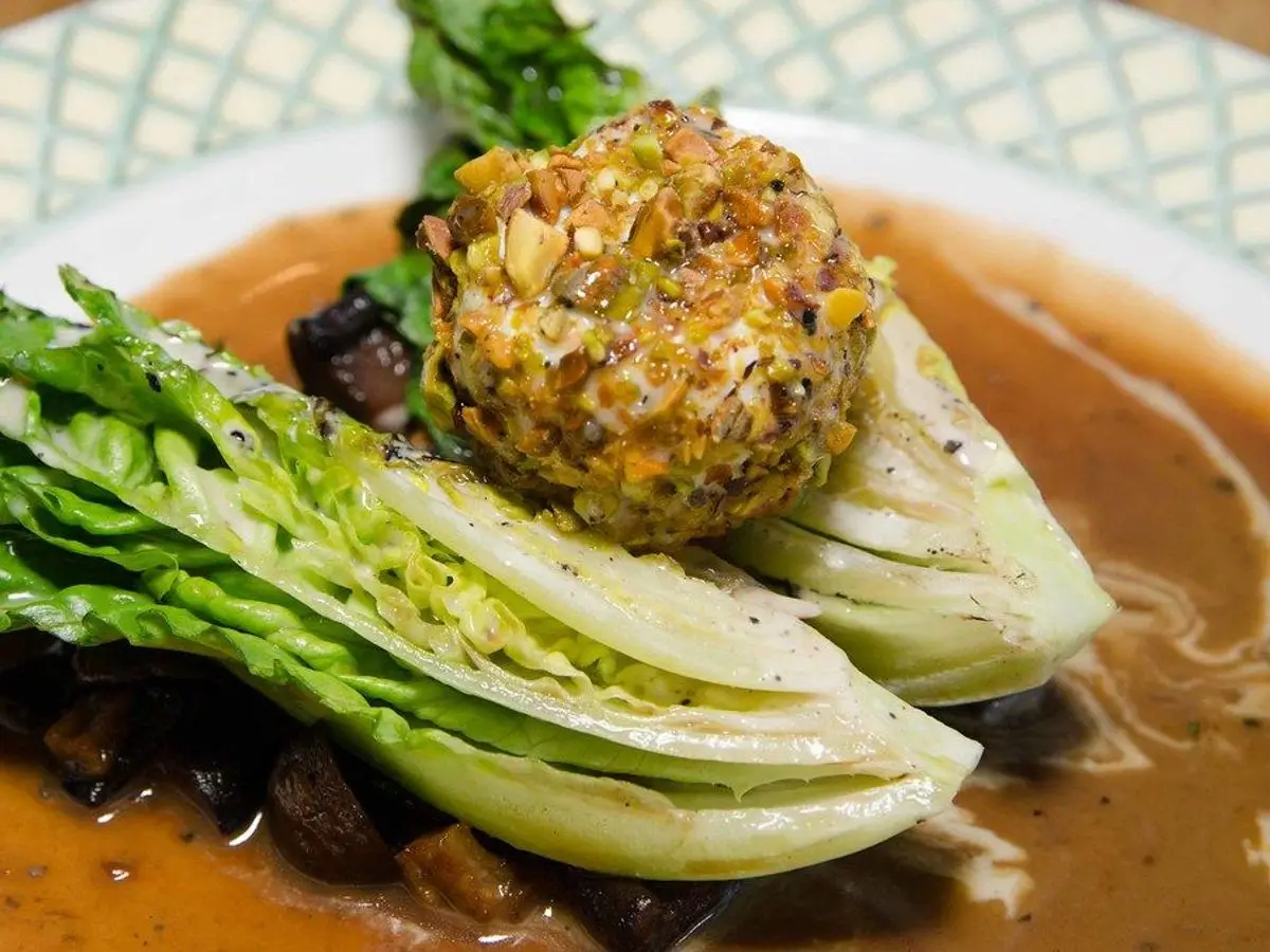 Bola de queso fresco rebozada en pistacho picado sobre cogollos de lechuga, en un plato con salsa