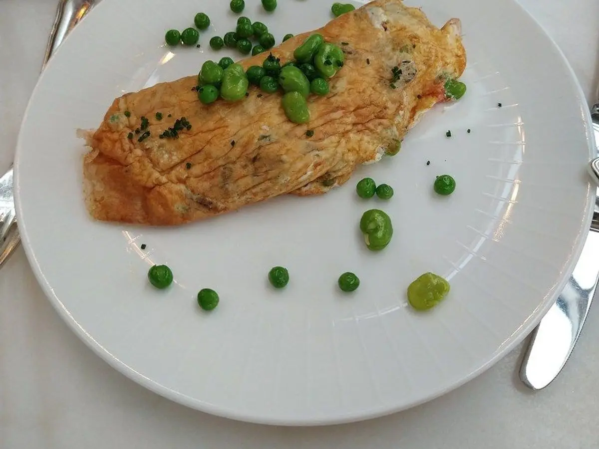 Tortilla francesa doblada con guisantes esparcidos sobre un plato blanco