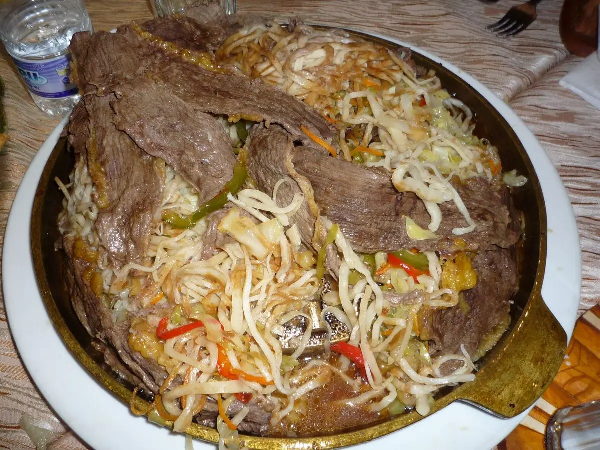 Fuente de fideos salteados con verduras y lonchas de carne de cordero por encima