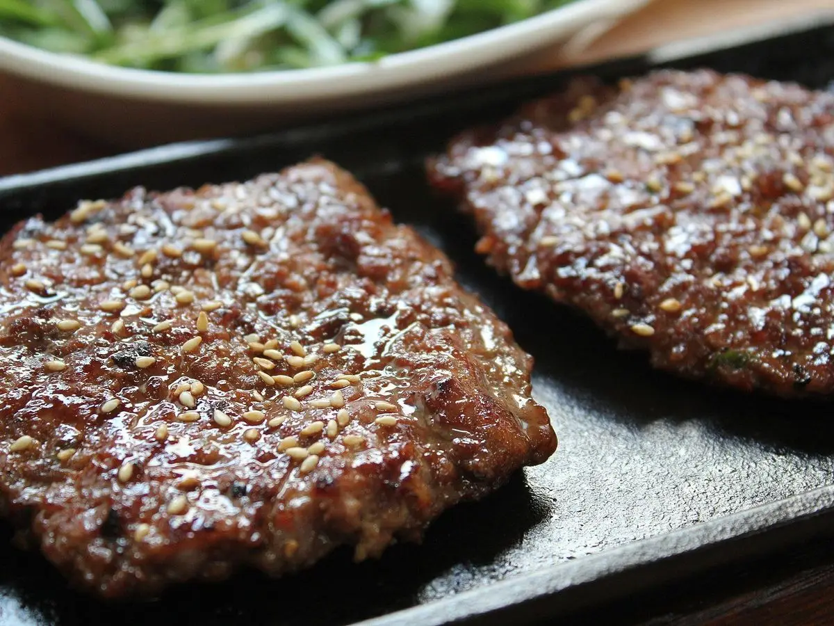 Dos hamburguesas de ternera glaseadas a la plancha sobre una bandeja de hierro negra