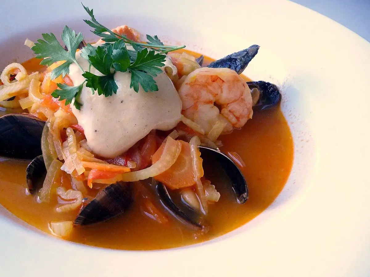 Plato hondo de sopa de pescado con mejillones, trozos de pescado, gambas, alioli y perejil