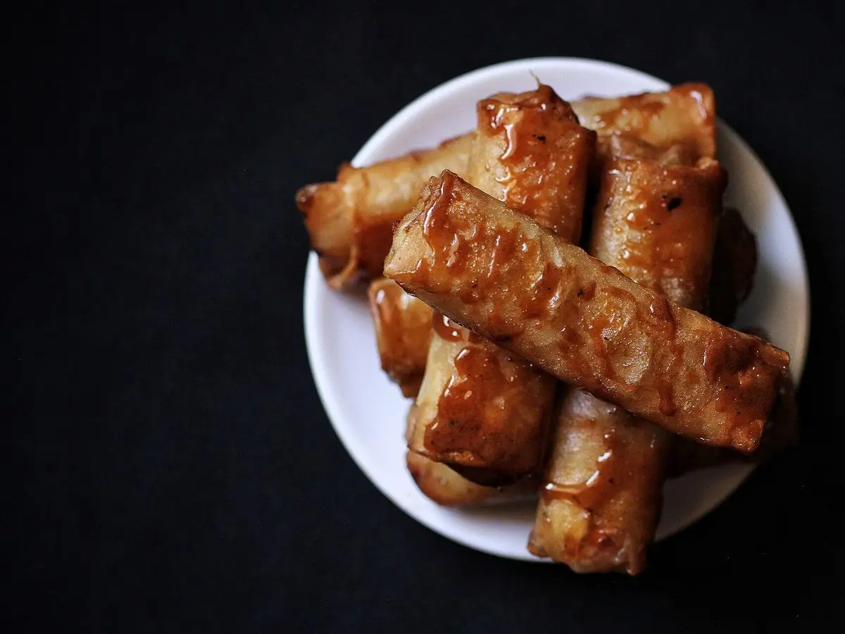 Plato blanco con rollitos de plátano fritos y dorados, envueltos en masa crujiente
