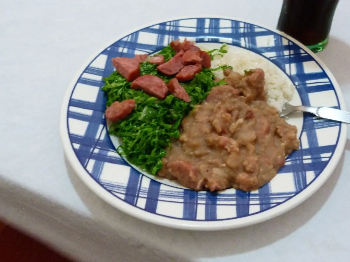 Plato de tutu de frijoles con embutido en rodajas, col verde salteada y arroz blanco