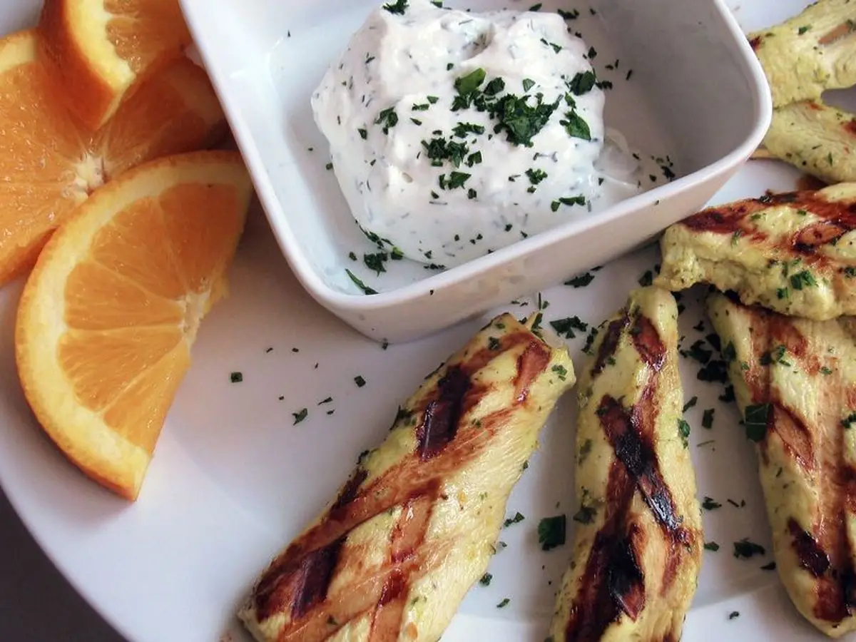 Bastones de calabacín a la plancha con salsa de yogur y hierbas, junto a rodajas de naranja