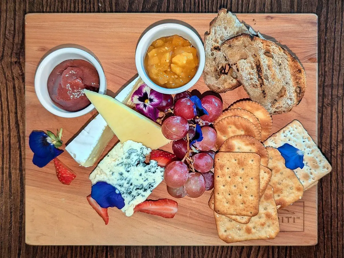 Tabla de madera con uvas, quesos, galletas saladas y mermeladas