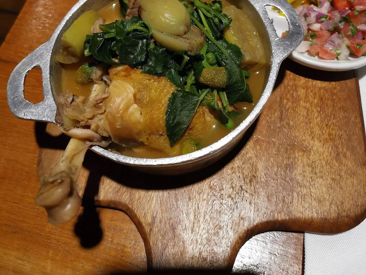 Cazuela de metal con guiso de verduras de hoja y pollo, con arroz y ensalada servidos al lado