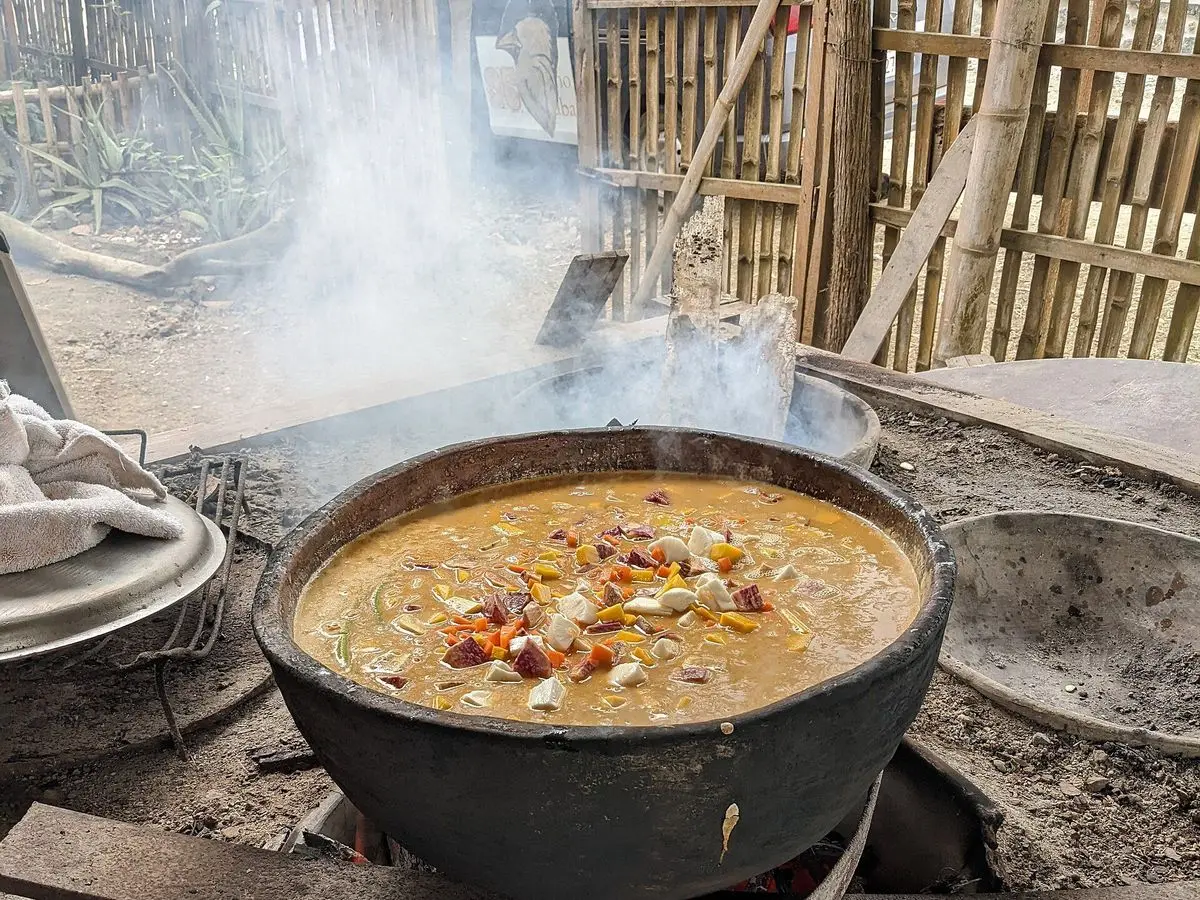 Olla negra con sopa espesa de pescado y cacahuete hirviendo sobre un horno de leña