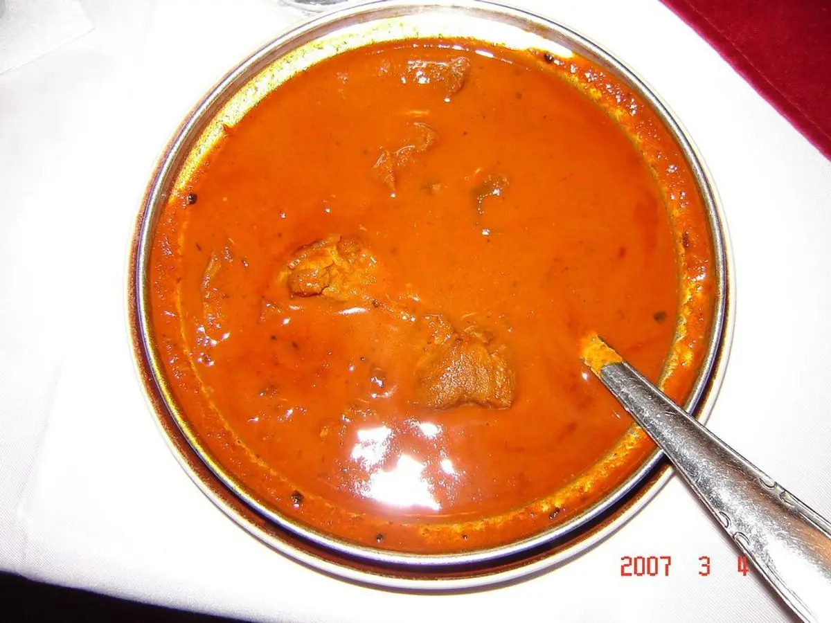 Cuenco de curry vindaloo de carne en salsa naranja intensa sobre un mantel blanco