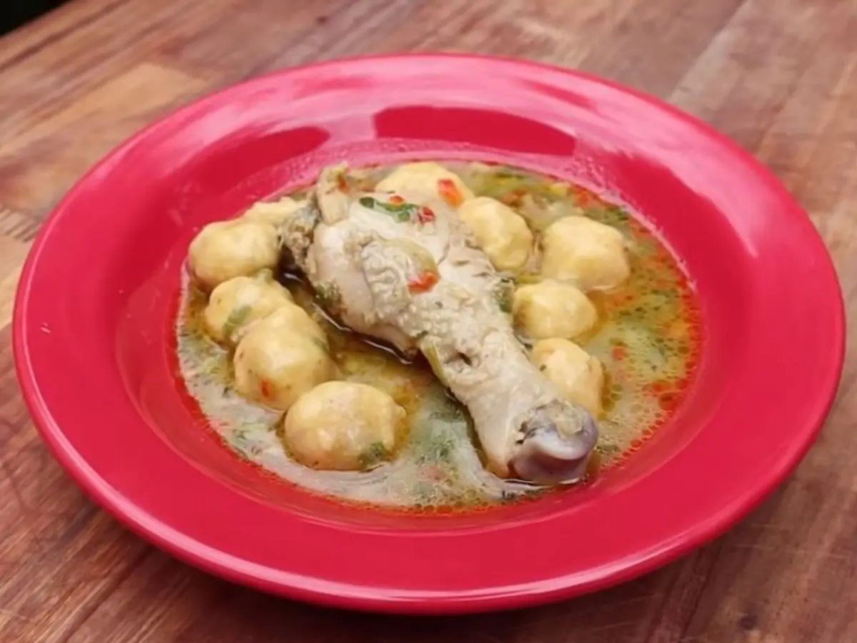 Plato rojo con sopa de muslo de pollo y bolitas de harina de maíz y queso