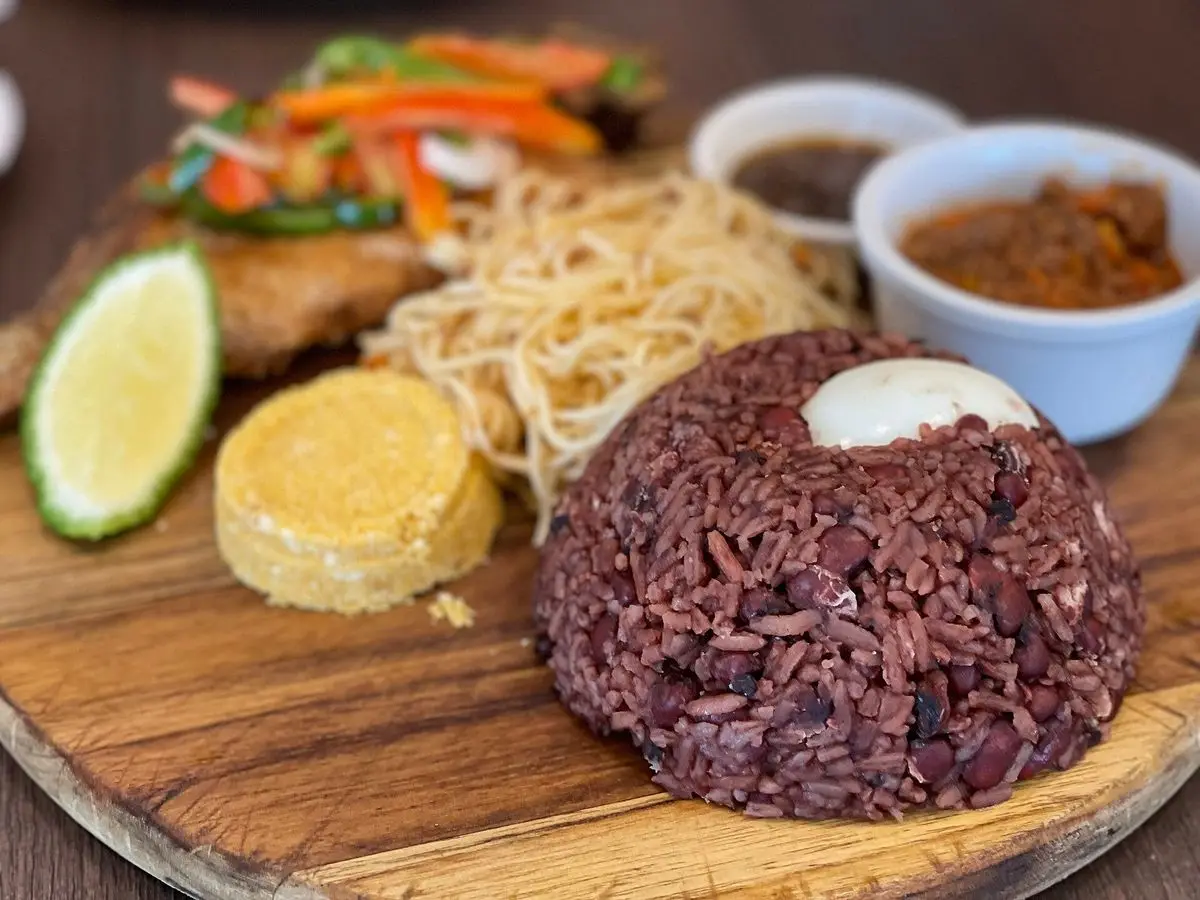 Montón de arroz rojizo con alubias sobre tabla de madera con espaguetis, lima y cuencos de salsa picante