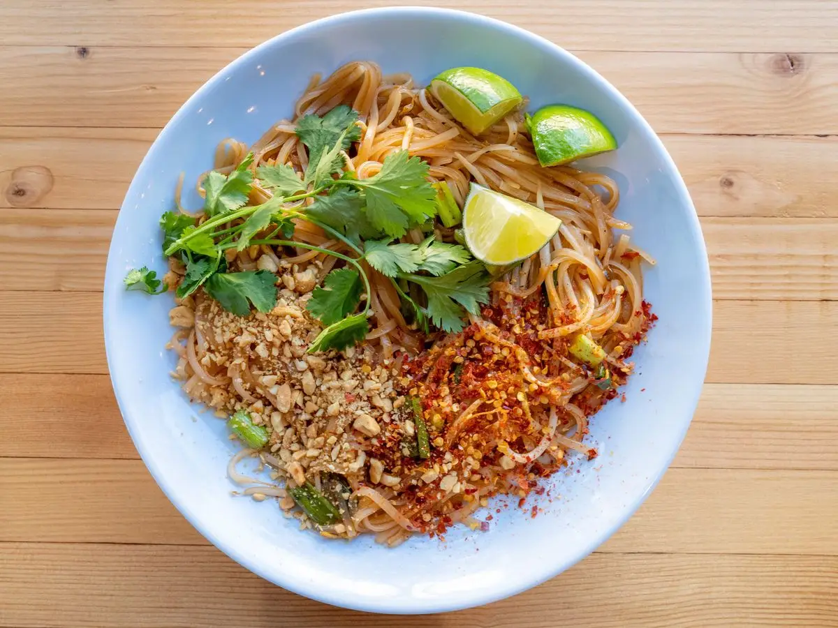 Bol de fideos de arroz salteados con cacahuetes picados, cilantro, guindilla y gajos de lima