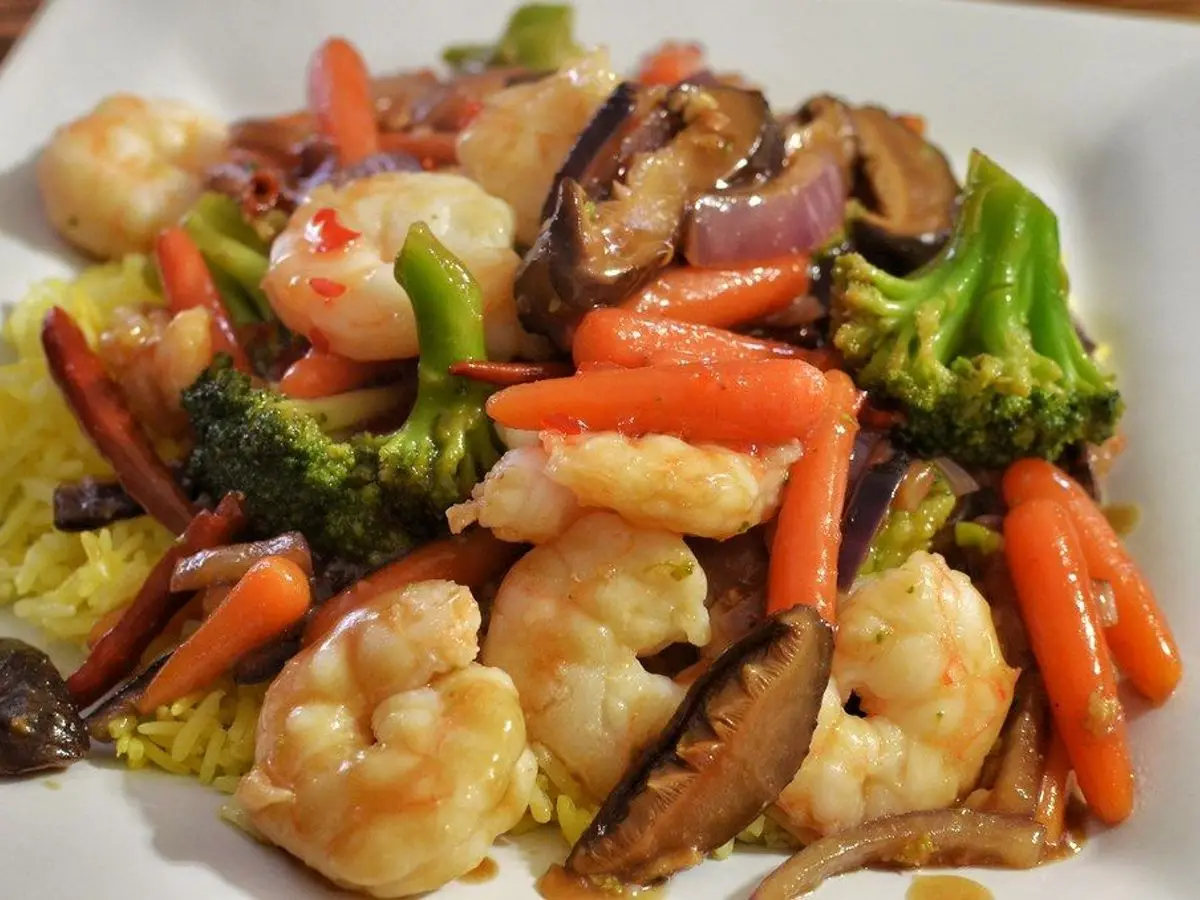 Salteado de langostinos con brócoli, zanahoria y setas shiitake en un plato blanco