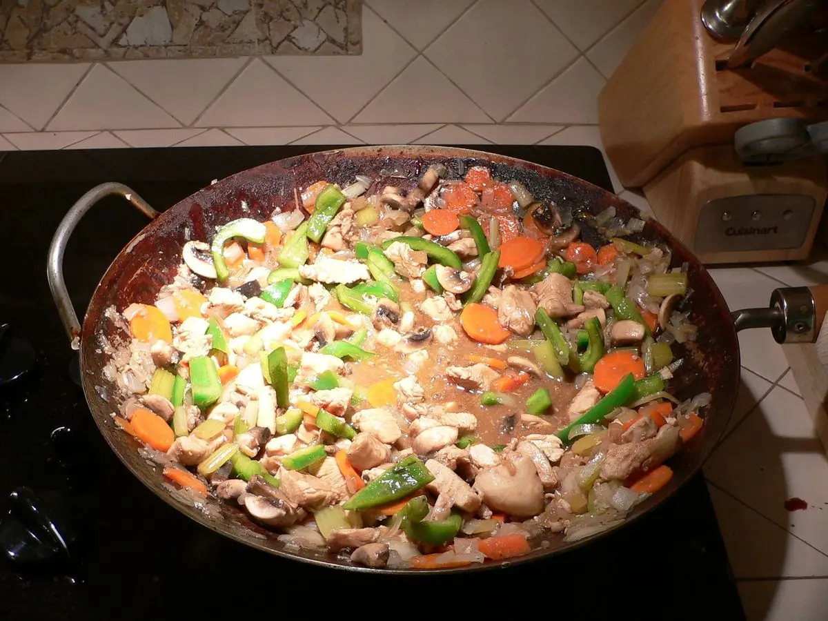 Wok de acero con pollo salteado, setas, col y verduras de colores sobre una placa de cocina