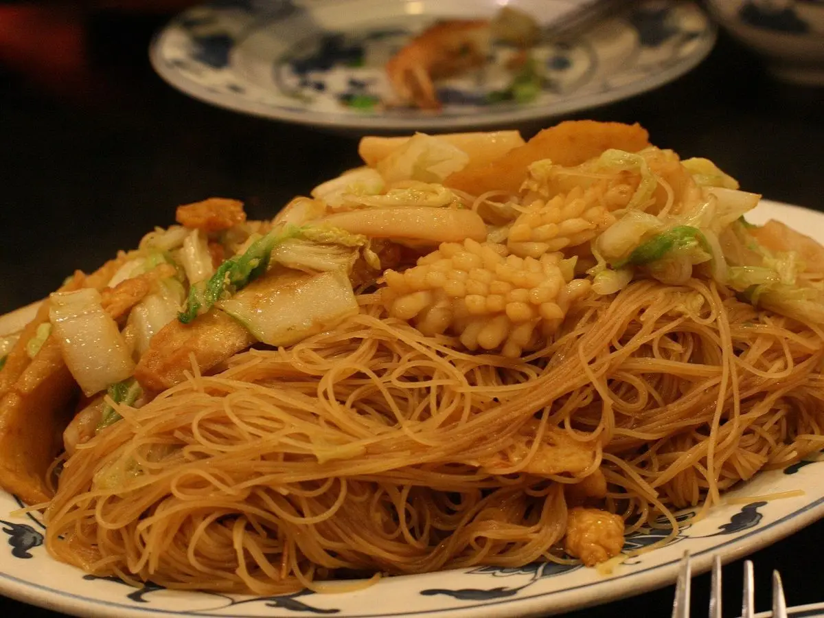 Fideos de arroz salteados al wok con trozos de pescado y marisco y verduras en un plato decorado