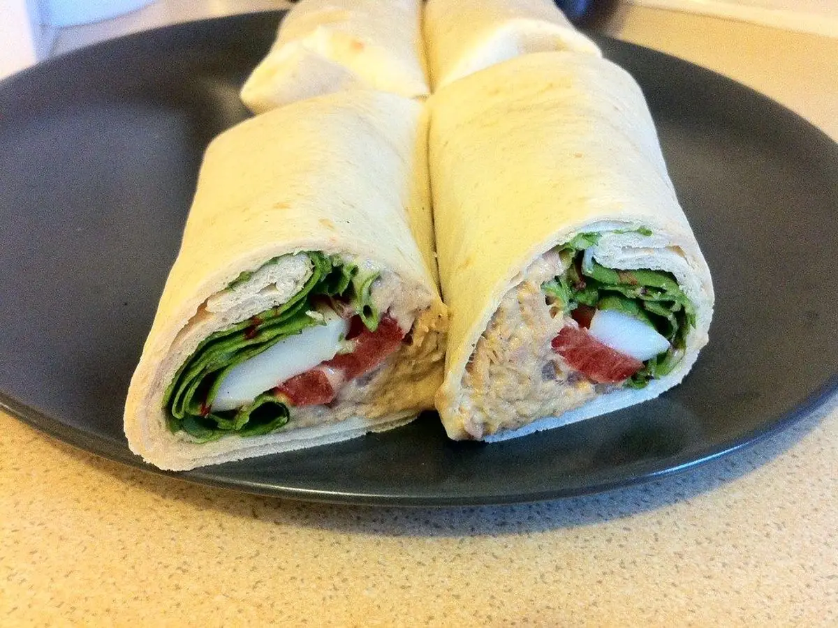 Wrap cortado por la mitad relleno de atún, hojas verdes y tomate sobre un plato negro