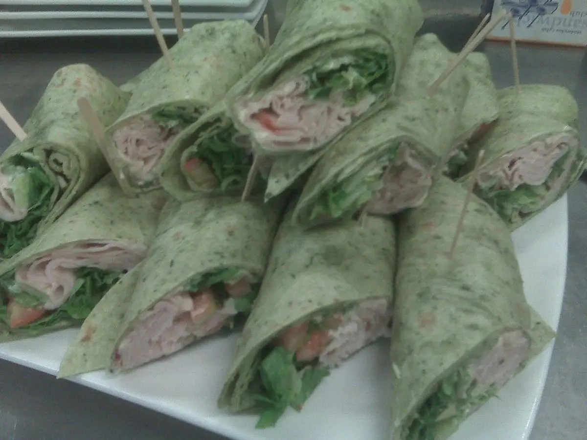 Rollitos de wrap de espinacas rellenos de pescado y hojas verdes, cortados en rodajas sobre un plato blanco