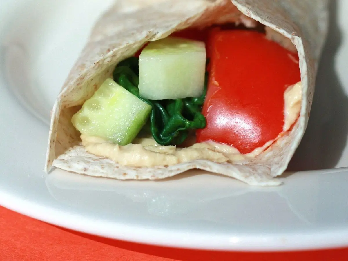 Wrap de tortilla enrollado relleno de pepino, espinacas y tomate rojo visto de cerca