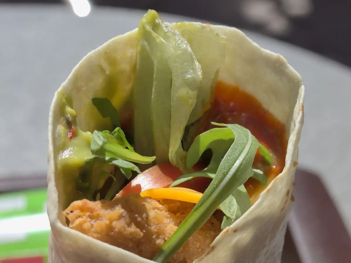 Wrap de pollo con rúcula, tomate y salsa visto de cerca, enrollado en tortilla