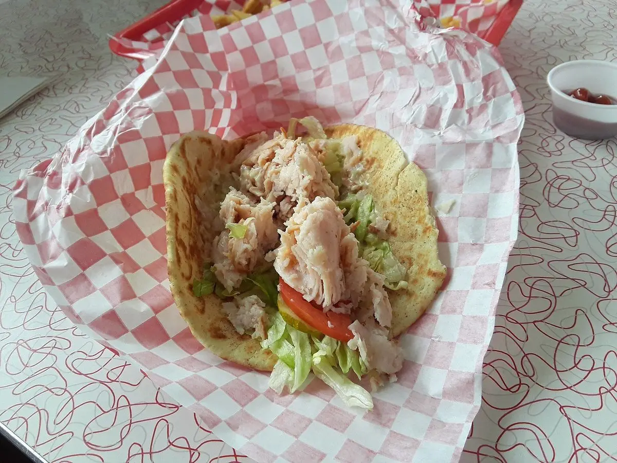 Wrap de tortilla relleno de carne desmenuzada, lechuga y tomate sobre papel a cuadros