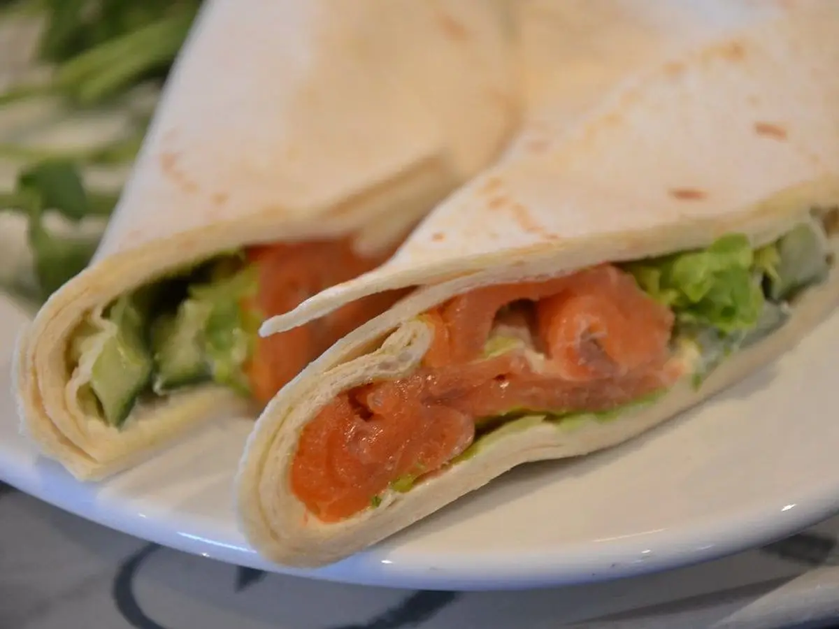 Dos mitades de wrap de tortilla rellenas de salmón, lechuga y pepino sobre un plato blanco