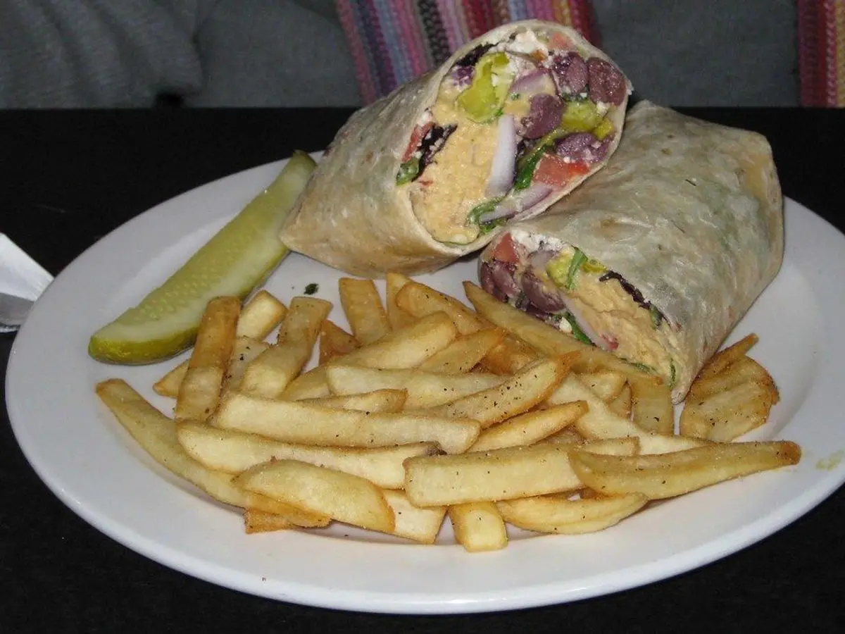 Wrap relleno de hummus y verduras cortado por la mitad, servido con patatas fritas