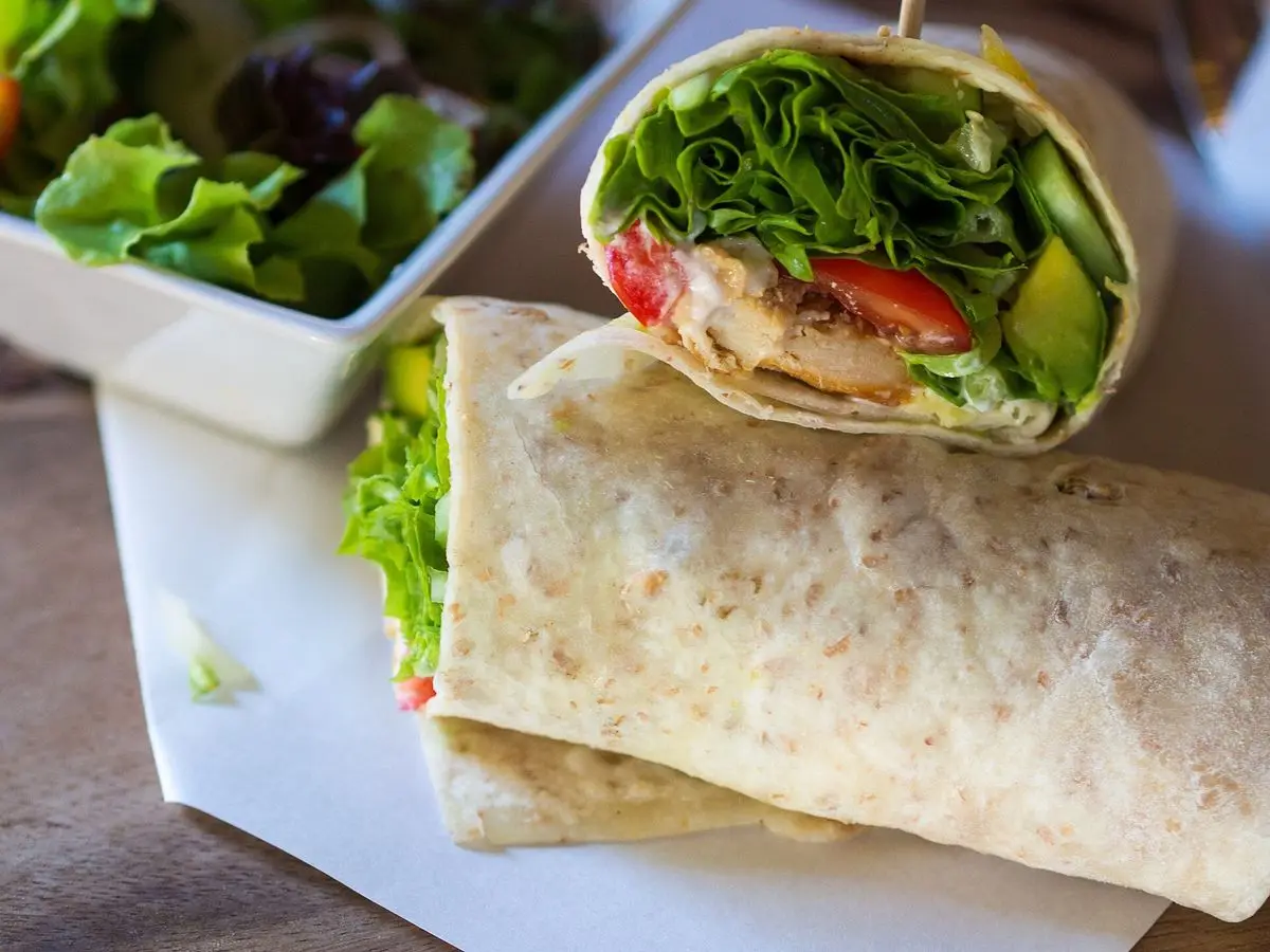 Wrap de pollo con rúcula, tomate y aguacate cortado por la mitad junto a una ensalada