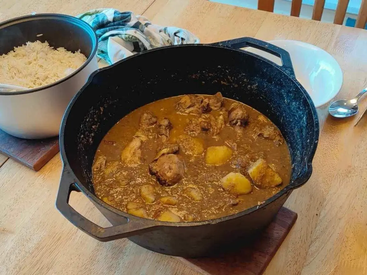 Cazuela negra de hierro con guiso de pollo y patata en salsa marrón y un cuenco de arroz al lado