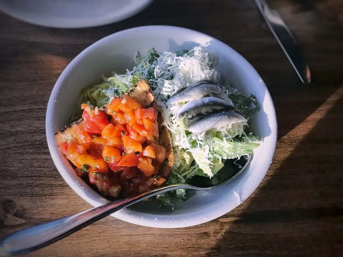 Cuenco de ensalada de hojas verdes con salsa de tomate y pescado en filetes