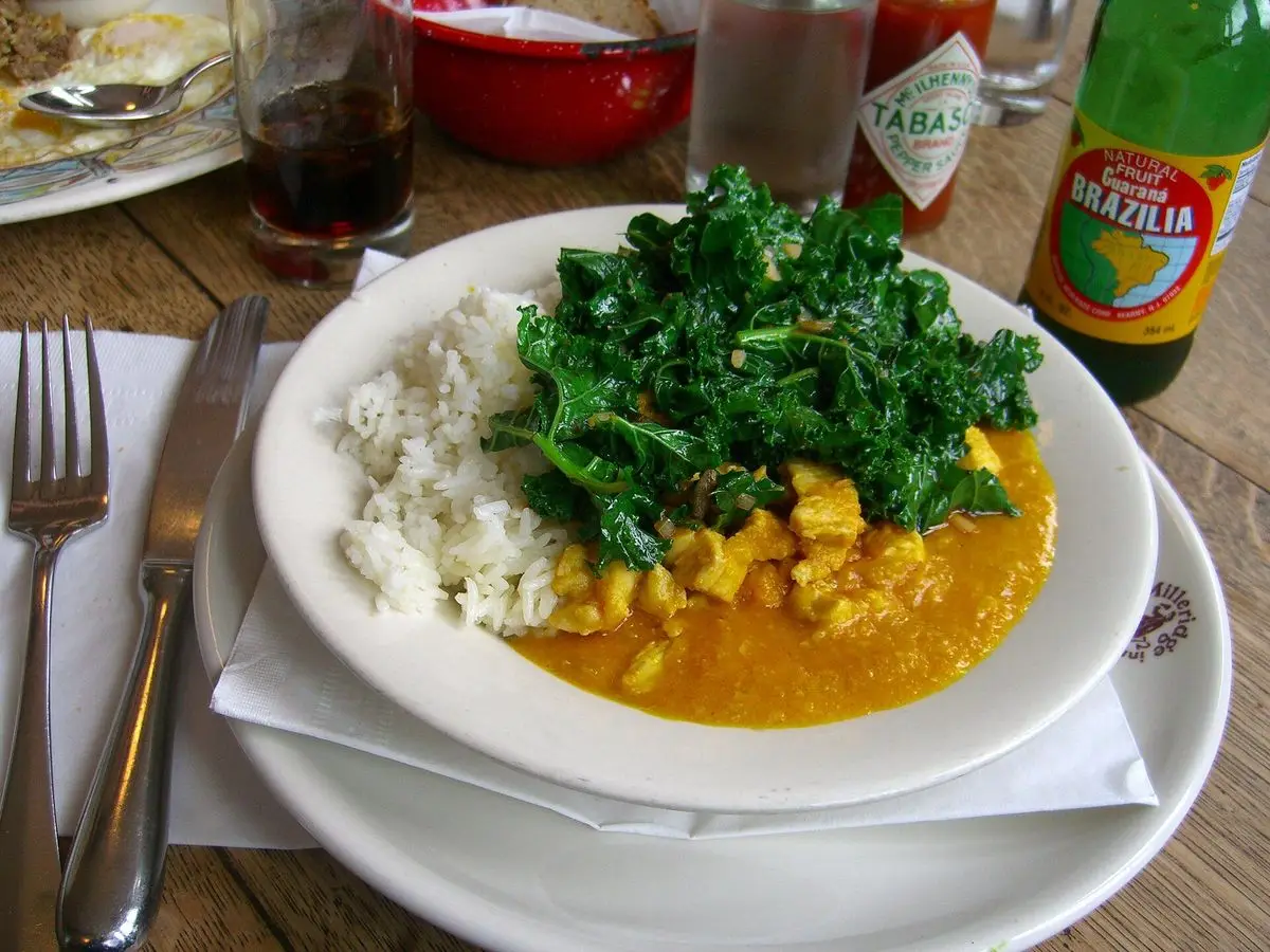 Plato blanco con pollo en salsa cremosa amarilla, arroz blanco y verdura de hoja salteada