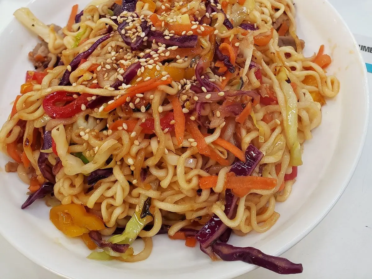 Plato blanco de fideos yakisoba salteados con col lombarda, zanahoria y sésamo