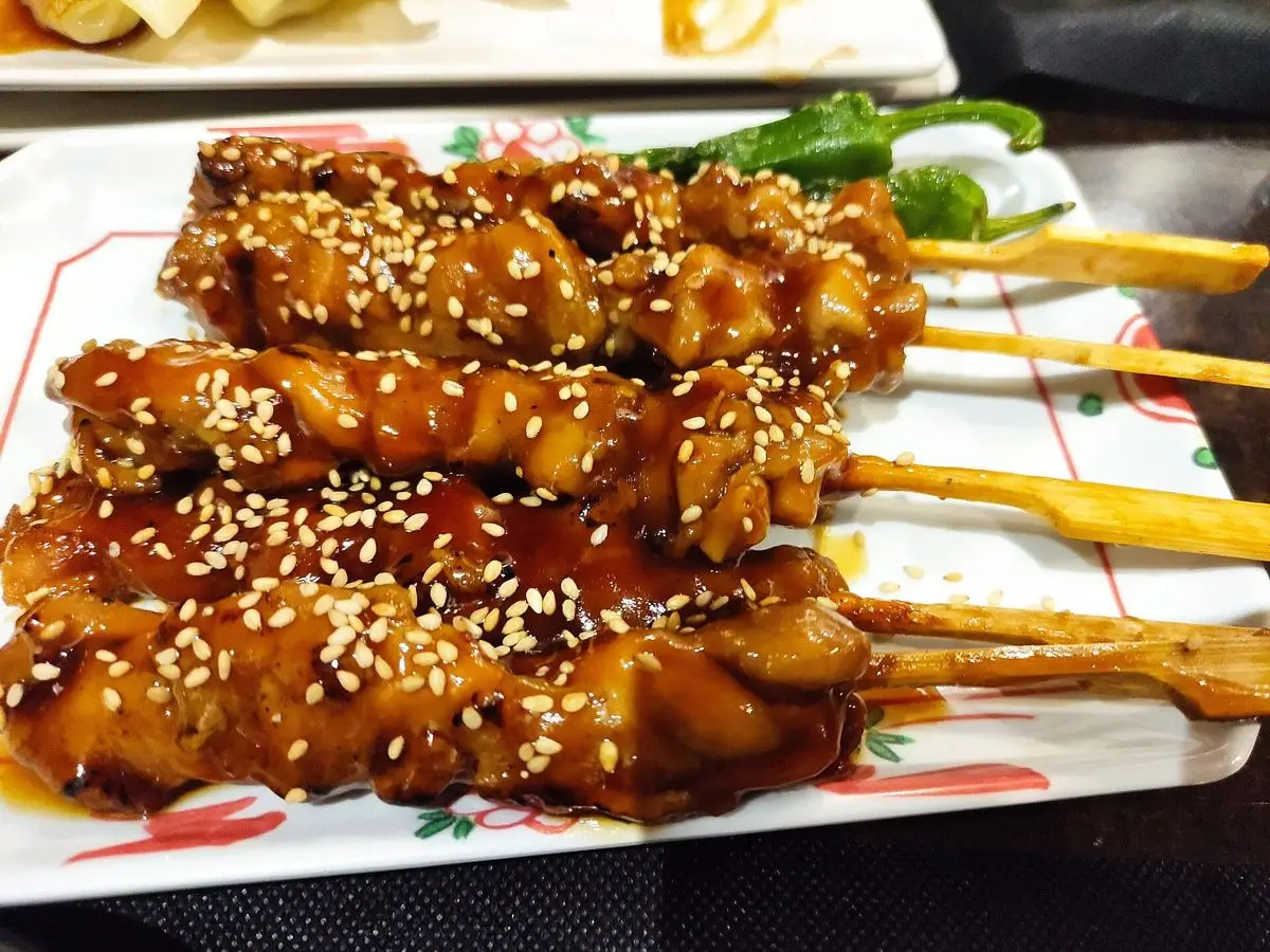 Brochetas de pollo glaseadas con semillas de sésamo sobre un plato, estilo yakitori