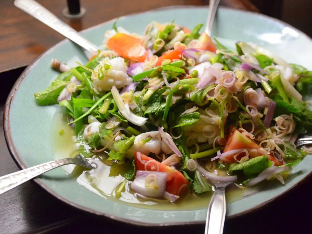 Plato de ensalada tailandesa picante con hierbas frescas, cebolla morada y trozos de marisco