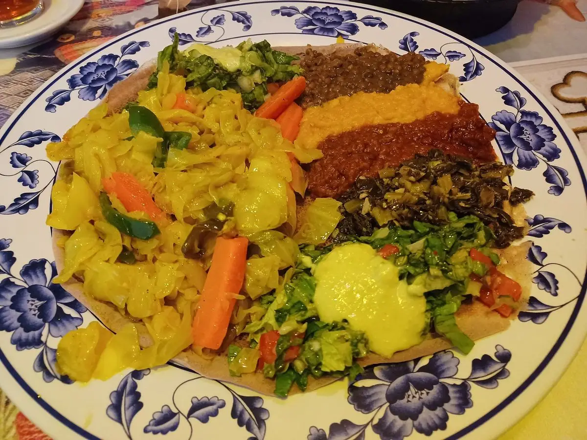 Plato con guiso suave amarillo de patata y zanahoria con cúrcuma sobre injera junto a otros guisos etíopes