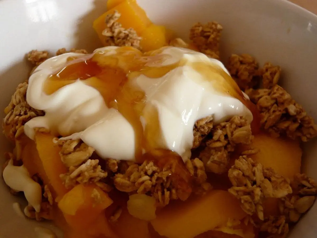 Cuenco de yogur espeso con granola crujiente, trozos de melocotón y un hilo de miel