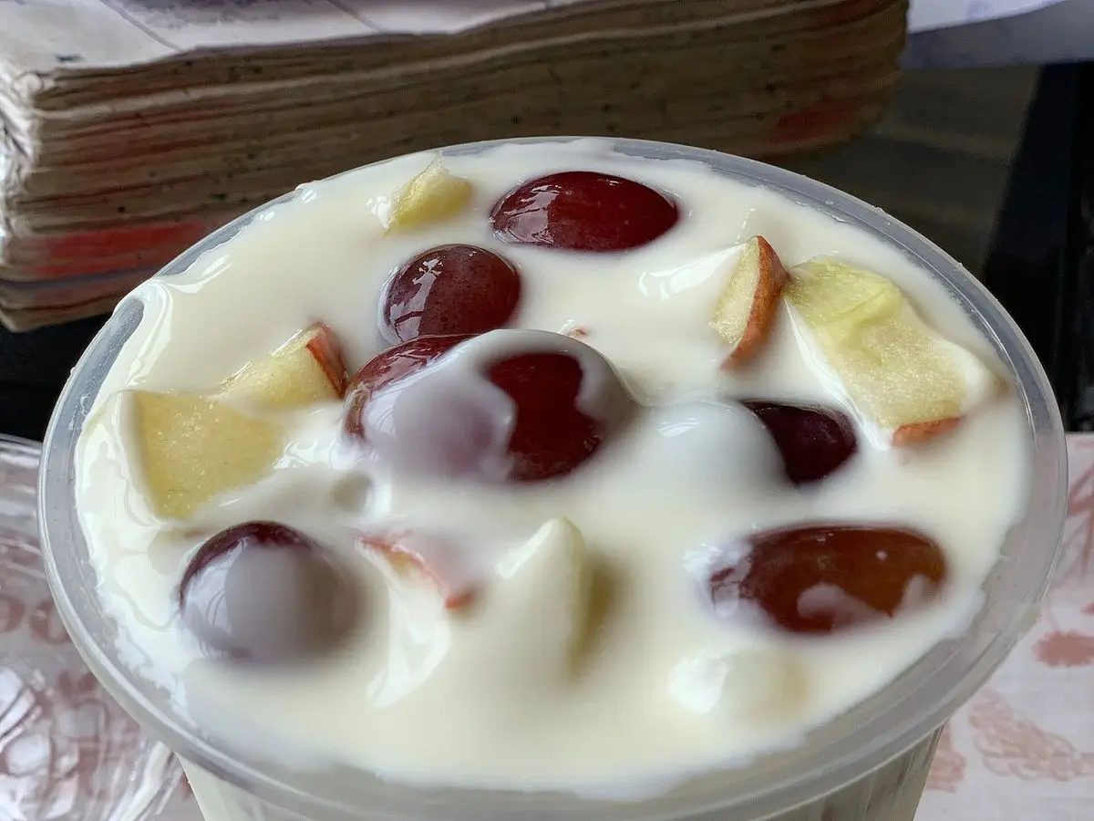 Vaso de yogur cremoso con trozos de fruta roja y amarilla