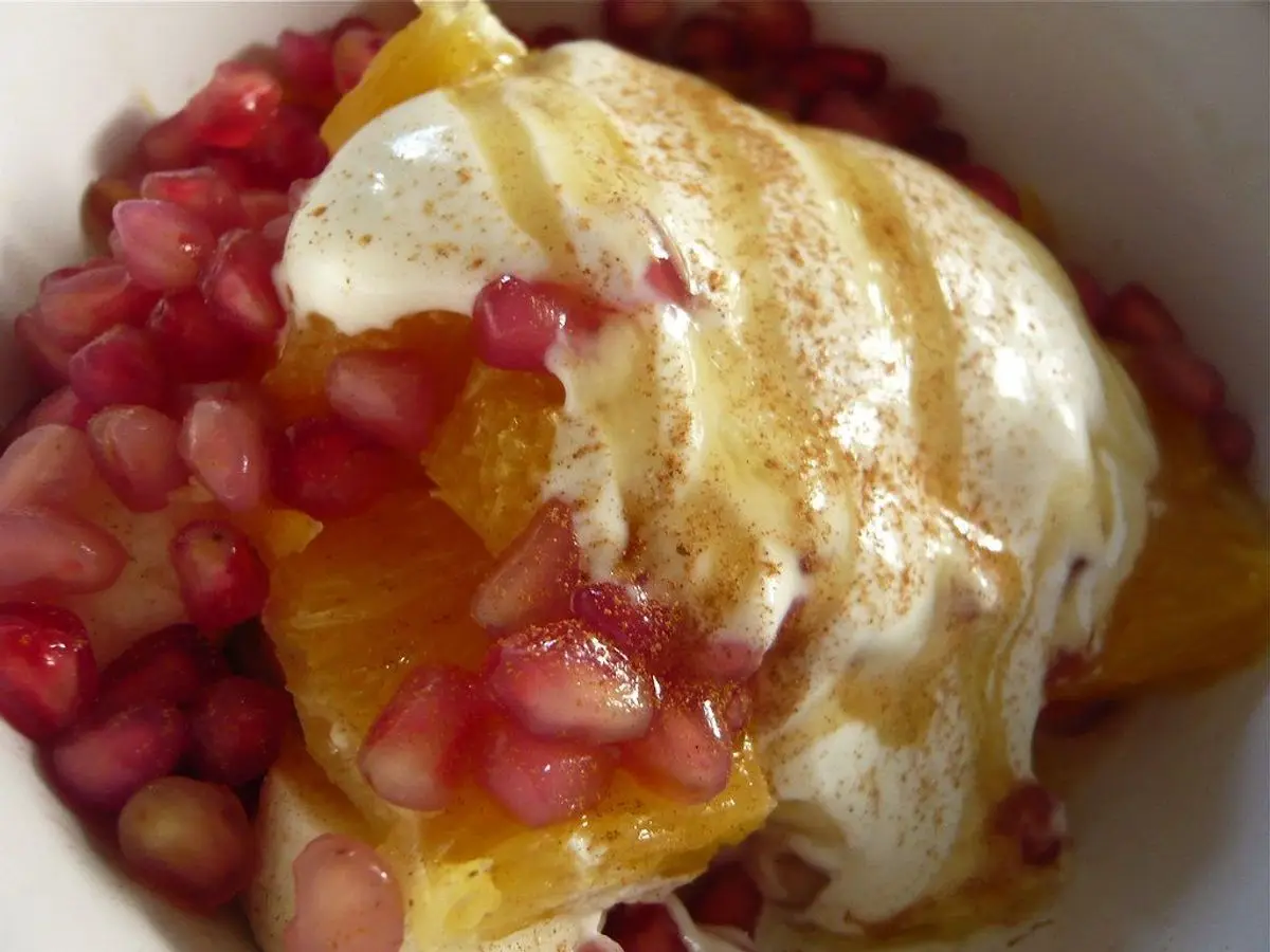 Yogur cremoso con granada, gajos de naranja y miel en un cuenco blanco