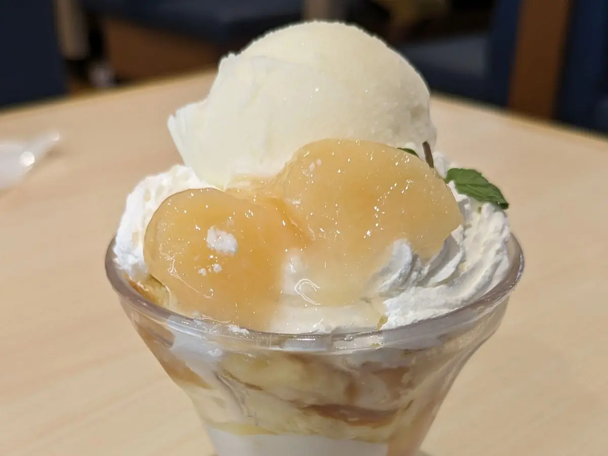 Copa de cristal con capas de yogur cremoso y melocotón sobre una superficie de madera