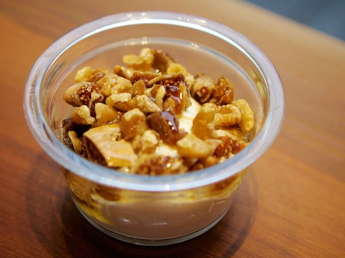 Vasito transparente de yogur cubierto de nueces e higos secos con miel sobre una mesa de madera